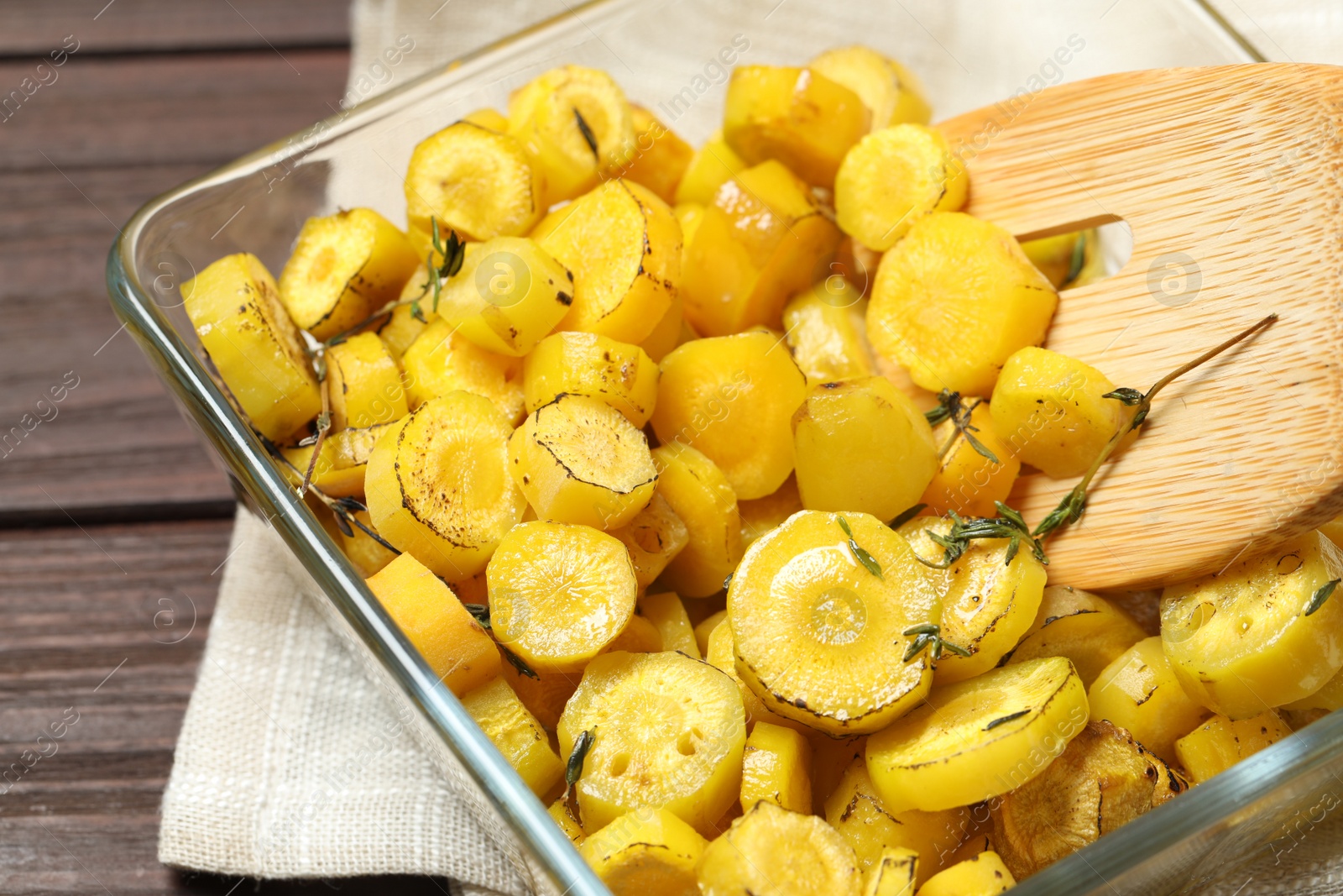 Photo of Baked yellow carrot and wooden fork in glass dish on table, closeup