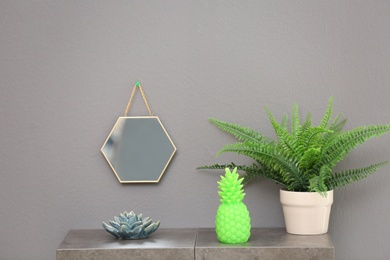 Stylish pineapple candle and houseplant on table against grey background