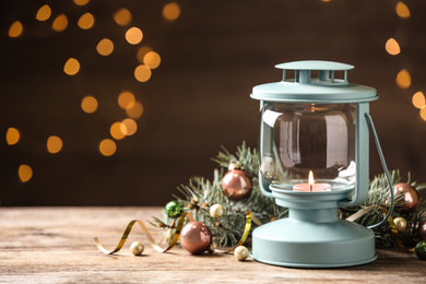 Photo of Lantern and Christmas decor on wooden table against blurred festive lights, space for text. Winter holiday