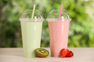 Photo of Plastic cups with different tasty smoothies and fresh fruits on wooden table outdoors