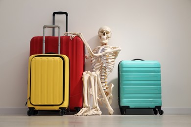 Waiting concept. Human skeleton with suitcases near light grey wall