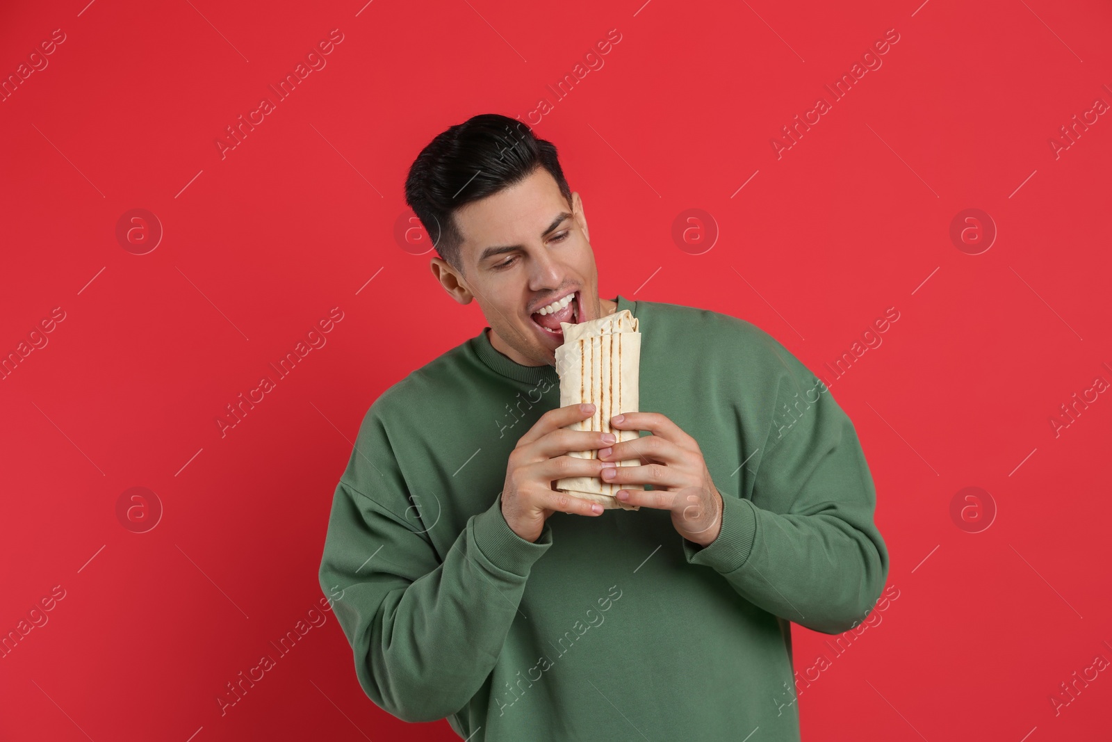 Photo of Man eating delicious shawarma on red background