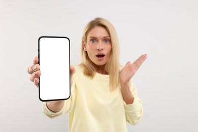 Surprised woman holding smartphone with blank screen on white background, selective focus