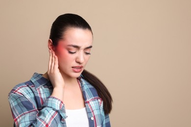 Image of Woman suffering from ear pain on beige background, space for text