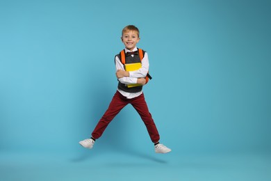 Photo of Happy schoolboy with backpack and books jumping on light blue background
