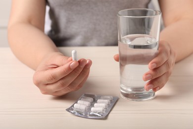 Woman with pill and glass of water at white wooden table, closeup