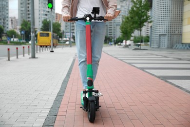 Photo of Man riding modern electric kick scooter on city street, closeup