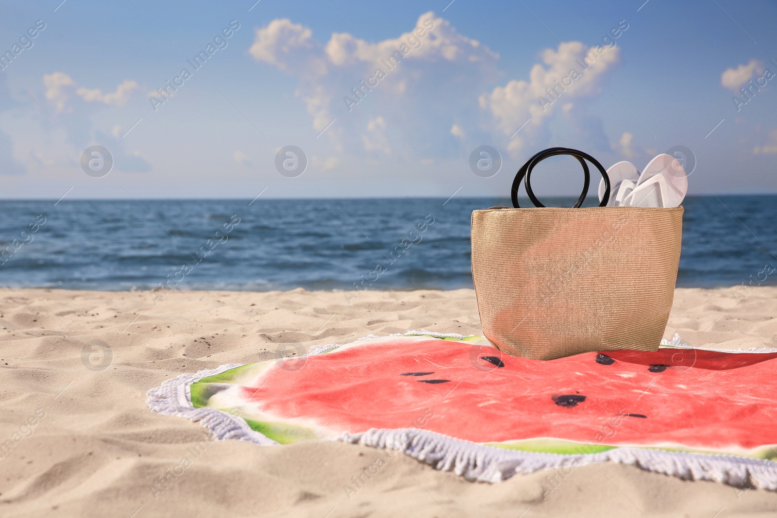 Photo of Beautiful watermelon beach towel with tassels, bag and flip flops on sandy seashore