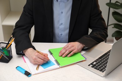 Photo of Man taking notes at white wooden table in office, closeup