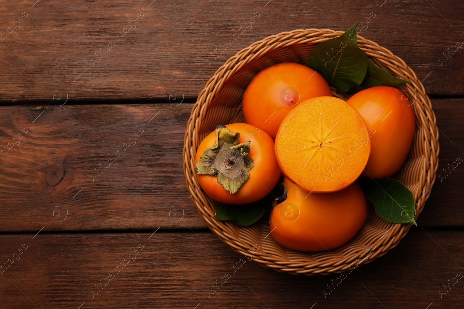 Photo of Delicious ripe persimmons in wicker basket on wooden table, top view. Space for text