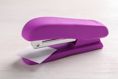 Photo of One new bright stapler with paper note on white wooden table, closeup