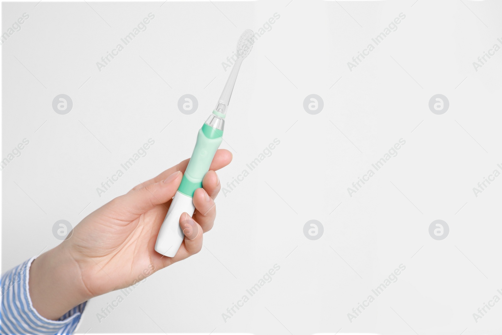 Photo of Woman holding electric toothbrush near white wall, closeup. Space for text