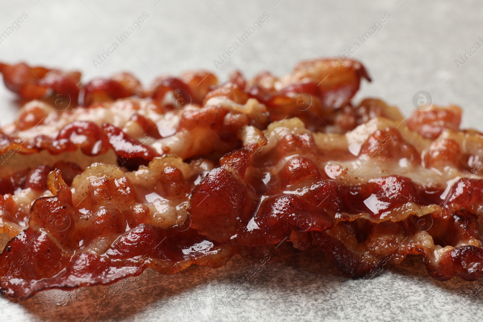 Photo of Pieces of tasty fried bacon on gray textured table, closeup