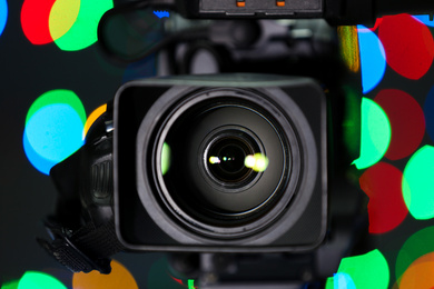 Photo of Modern video camera against blurred colorful lights, closeup