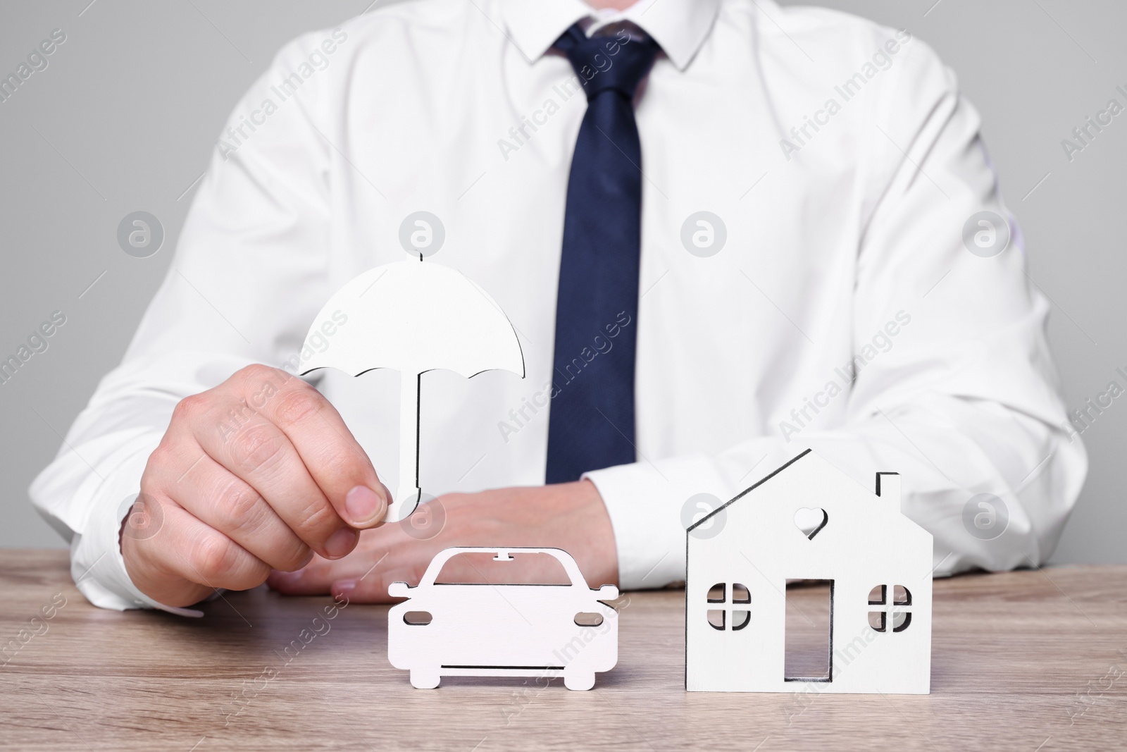 Photo of Man holding figure of umbrella above wooden table. closeup. Insurance concept