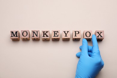 Photo of Doctor making word Monkeypox with wooden cubes on beige background, top view
