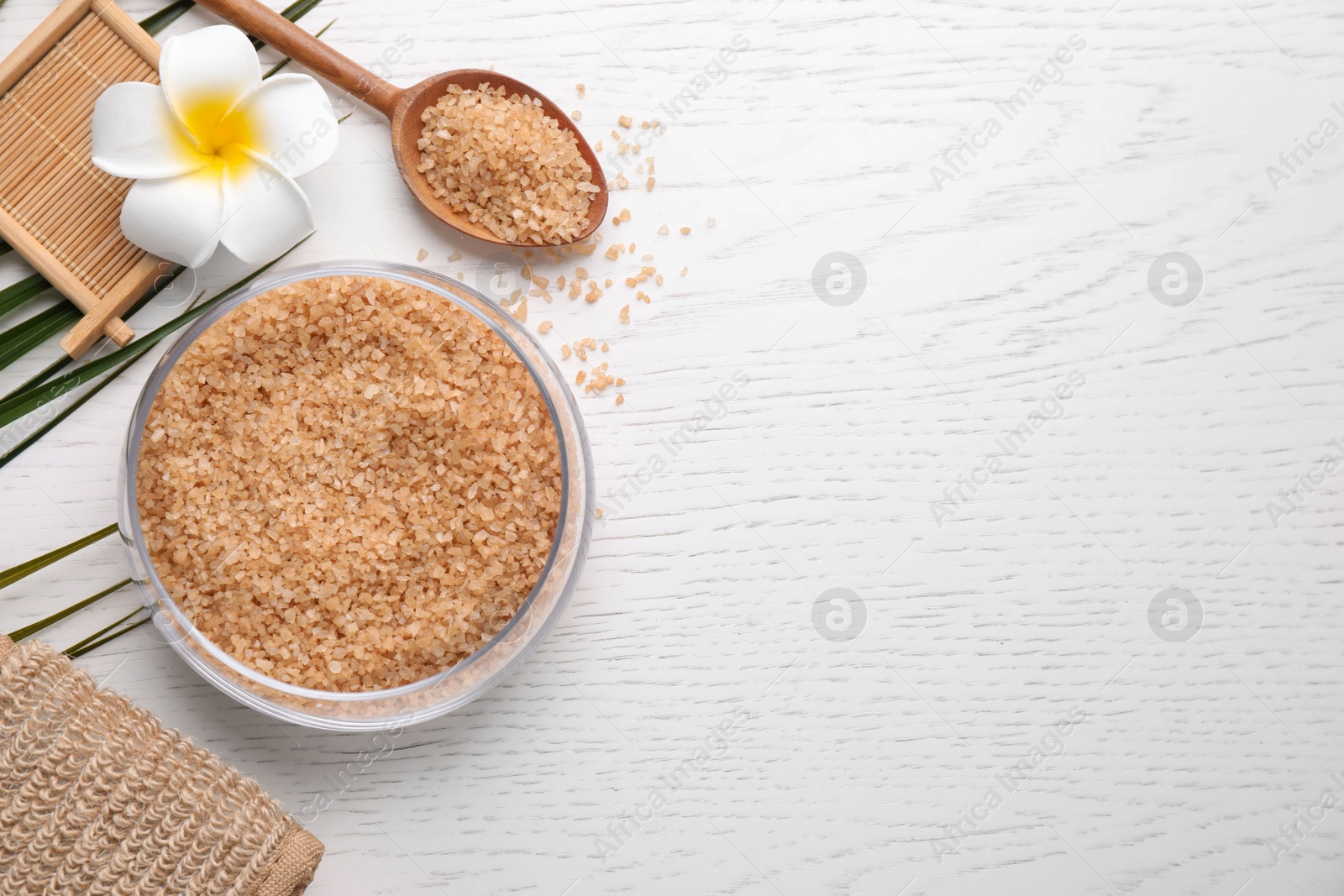 Photo of Flat lay composition with brown sea salt on white wooden background, space for text. Spa treatment