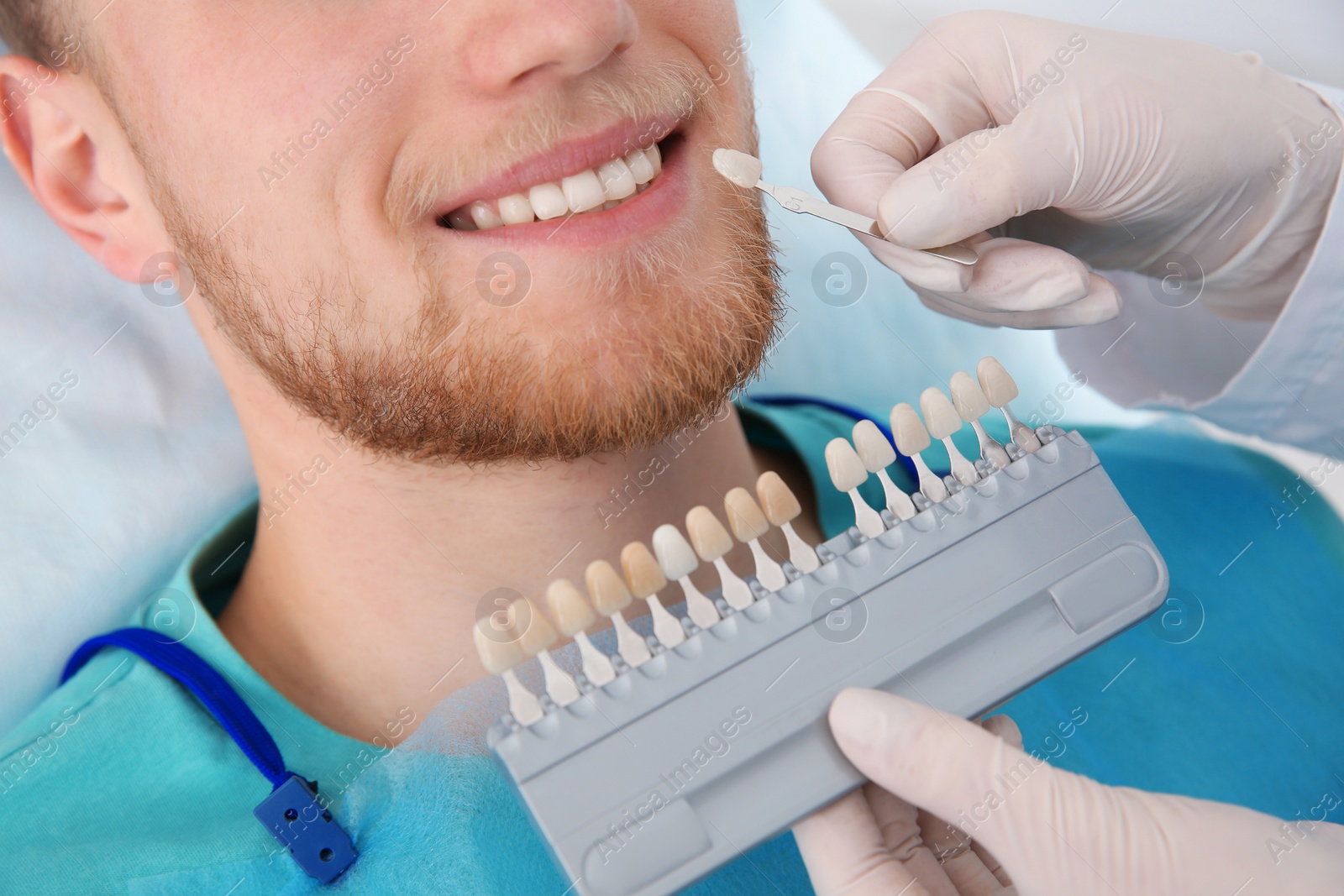 Photo of Dentist selecting patient's teeth color with palette in clinic, closeup