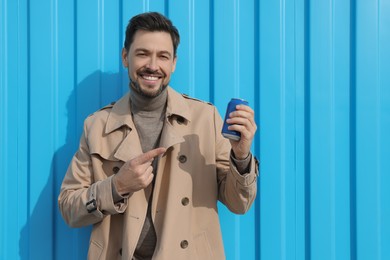 Handsome man holding tin can with beverage near light blue wall. Space for text