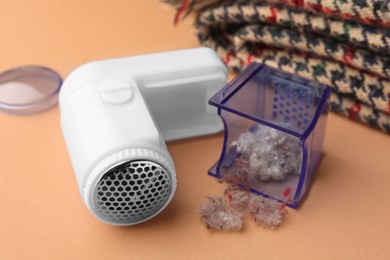 Modern fabric shaver with fuzz and scarf on pale orange background, closeup