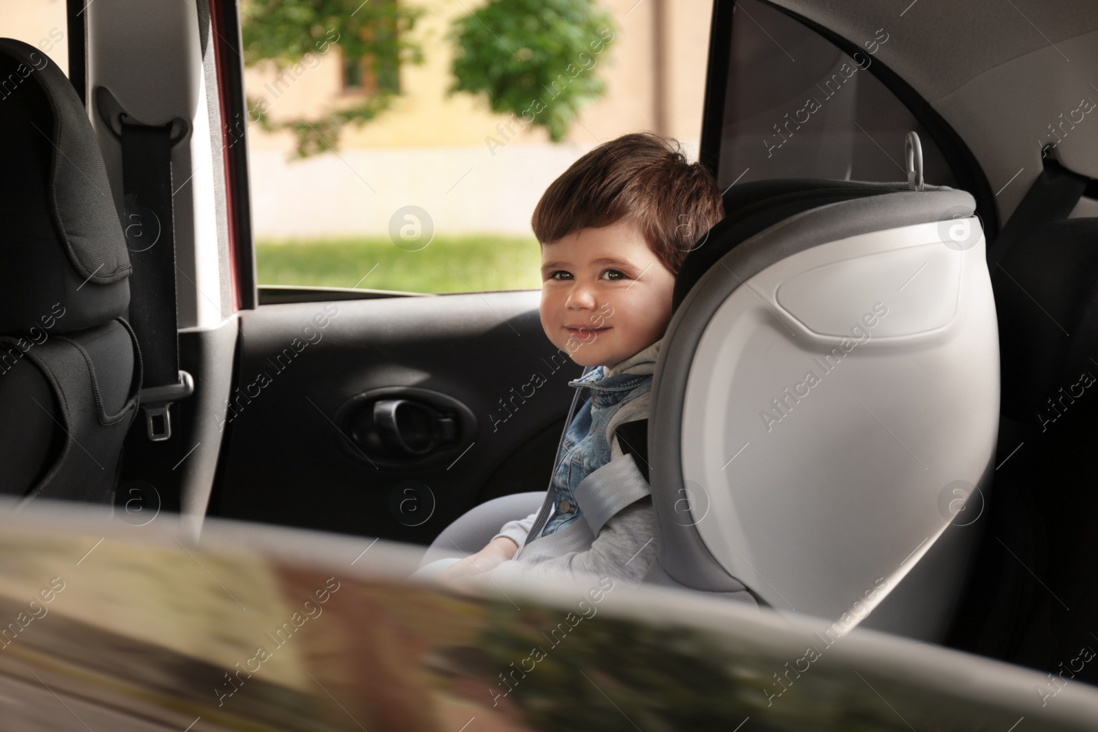 Photo of Cute little child sitting in safety seat inside car. Danger prevention