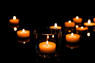 Photo of Beautiful burning wax candles on black background