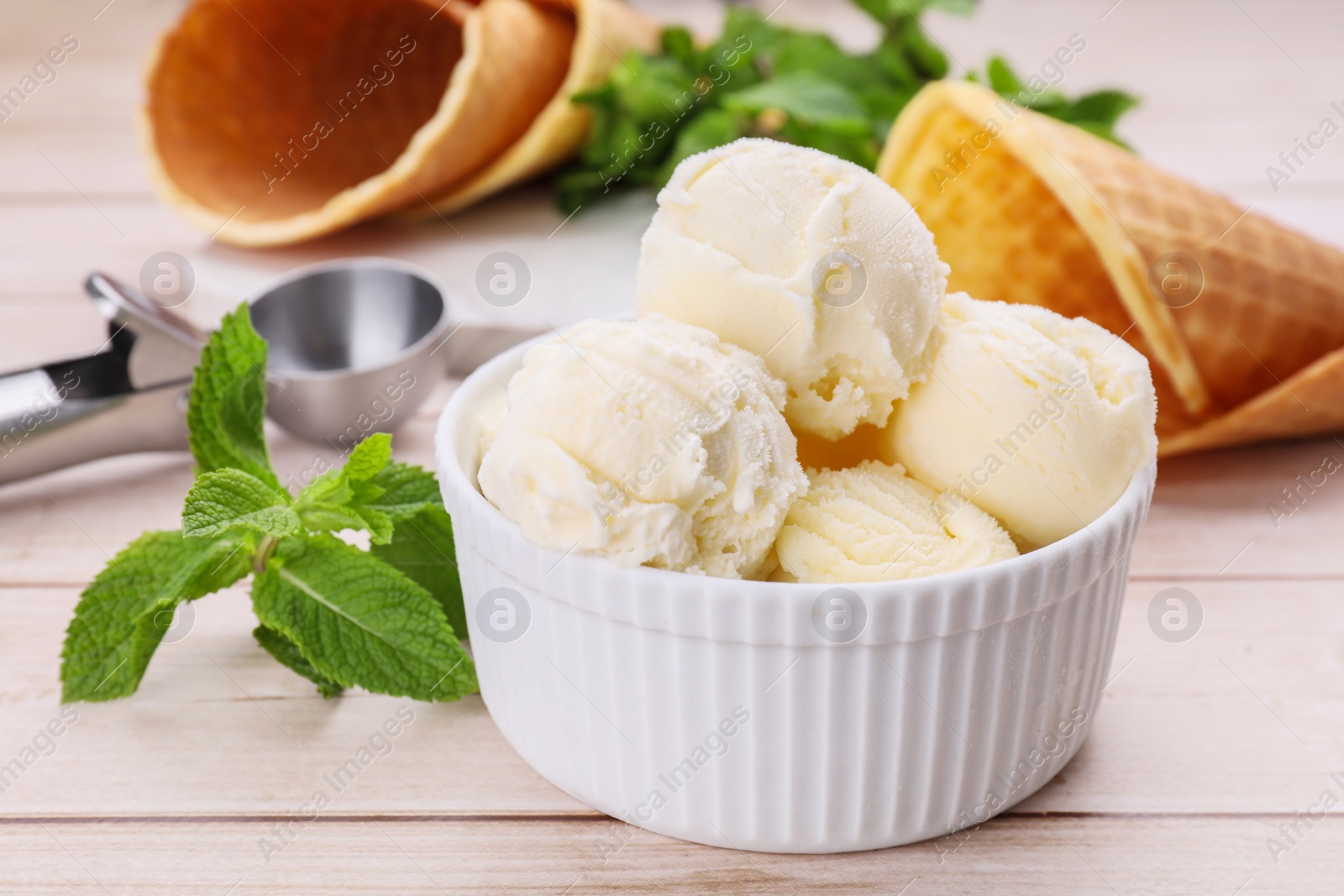 Photo of Bowl of ice cream and mint leaves on light wooden table, closeup