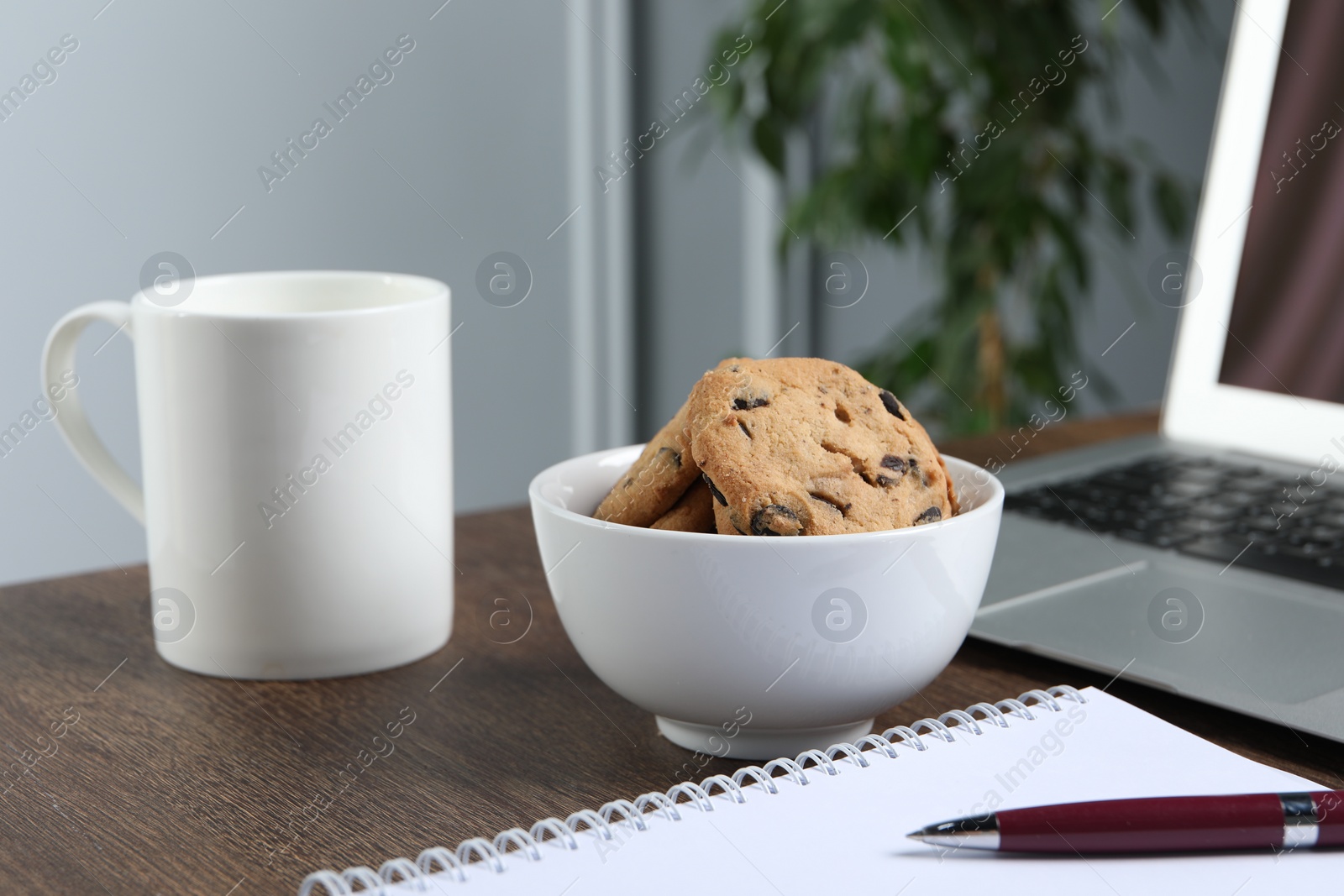 Photo of Chocolate chip cookies, mug and laptop on wooden table in office