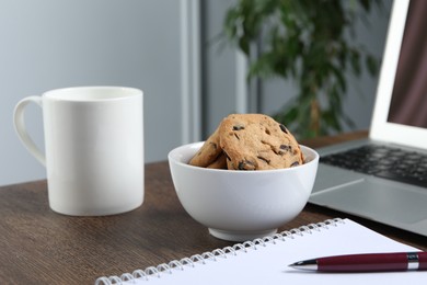 Photo of Chocolate chip cookies, mug and laptop on wooden table in office