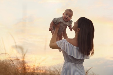 Photo of Happy mother with adorable baby in field at sunset, space for text