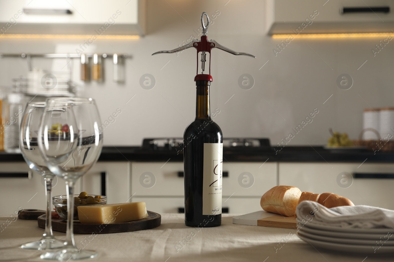 Photo of Wine bottle with corkscrew, wineglasses and food on table in kitchen