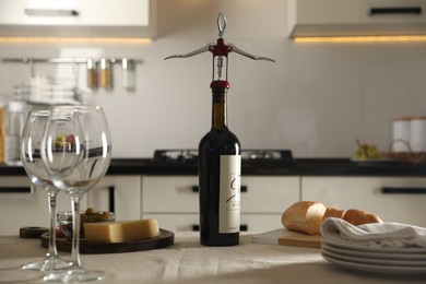 Wine bottle with corkscrew, wineglasses and food on table in kitchen