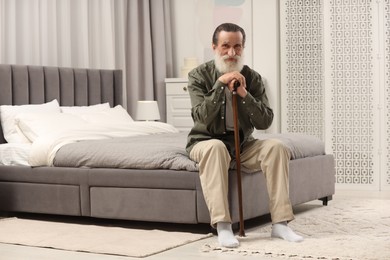 Senior man with walking cane on bed at home