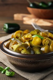 Bowl with slices of pickled green jalapeno peppers on wooden table, closeup