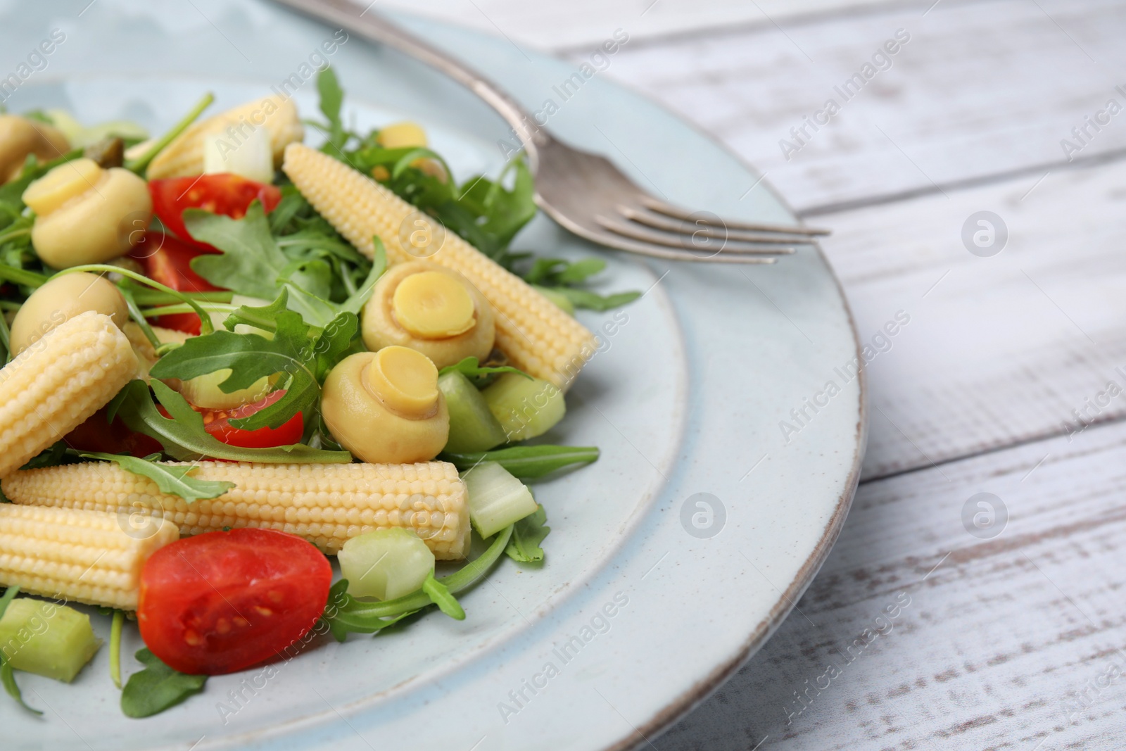 Photo of Tasty baby corn with vegetables, arugula and mushrooms on white wooden table, closeup