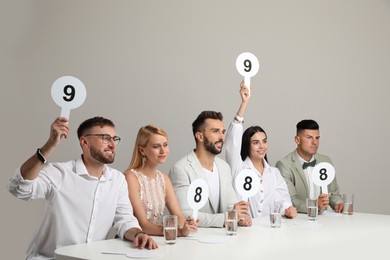 Photo of Panel of judges holding different score signs at table on beige background