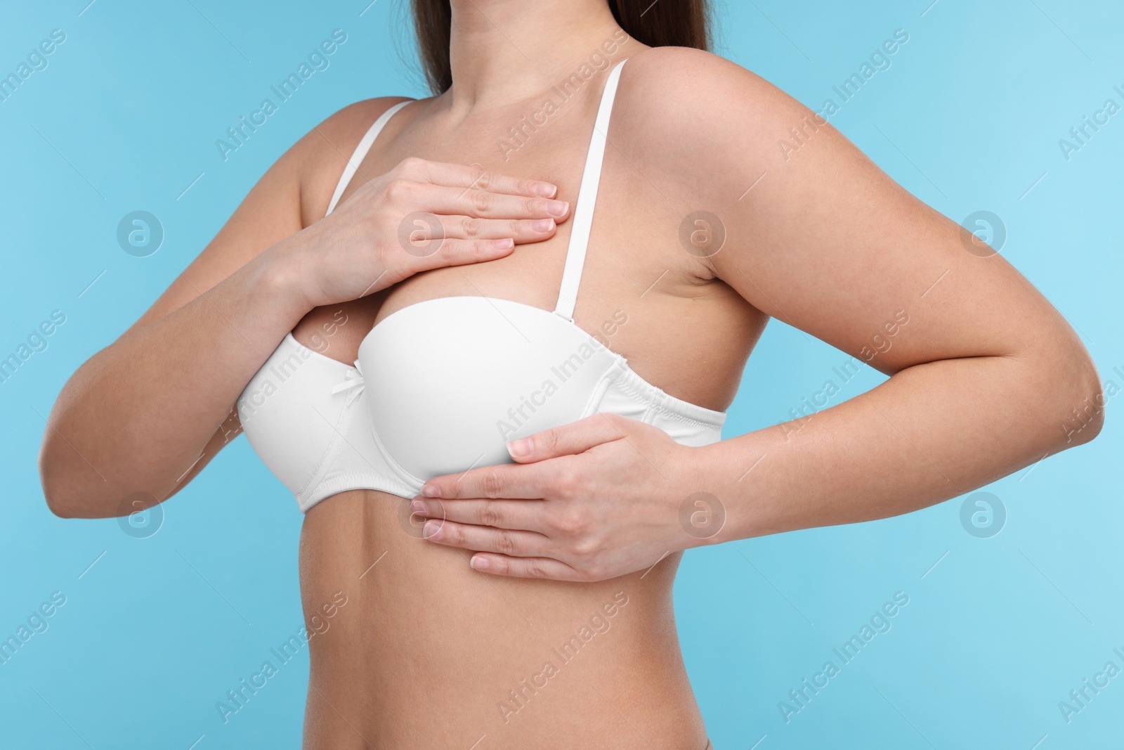 Photo of Mammology. Woman in bra doing breast self-examination on light blue background, closeup