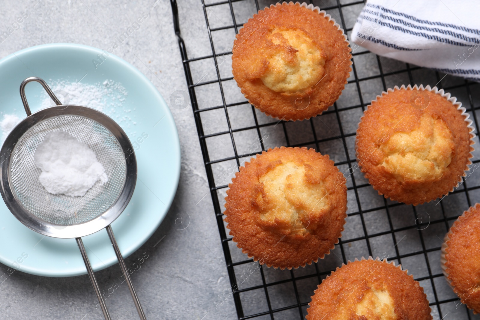 Photo of Delicious sweet muffins, plate and sieve on grey textured table, flat lay