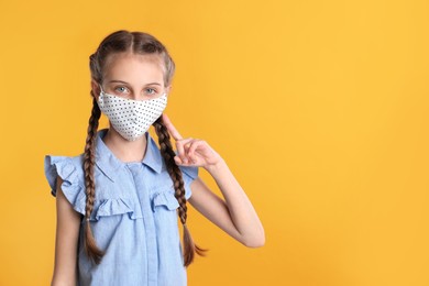 Photo of Girl wearing protective mask on yellow background, space for text. Child's safety from virus