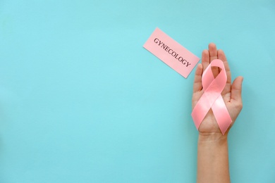 Photo of Woman holding symbolic ribbon of breast cancer awareness on color background, top view. Gynecological care