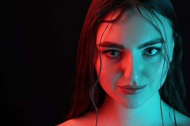 Portrait of beautiful woman in neon lights against black background, closeup. Space for text
