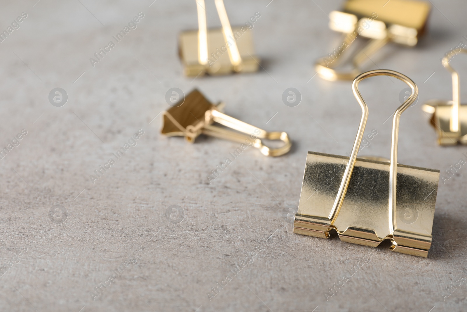 Photo of Golden binder clips on grey stone table, closeup. Space for text