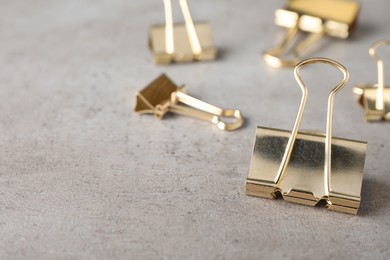 Golden binder clips on grey stone table, closeup. Space for text