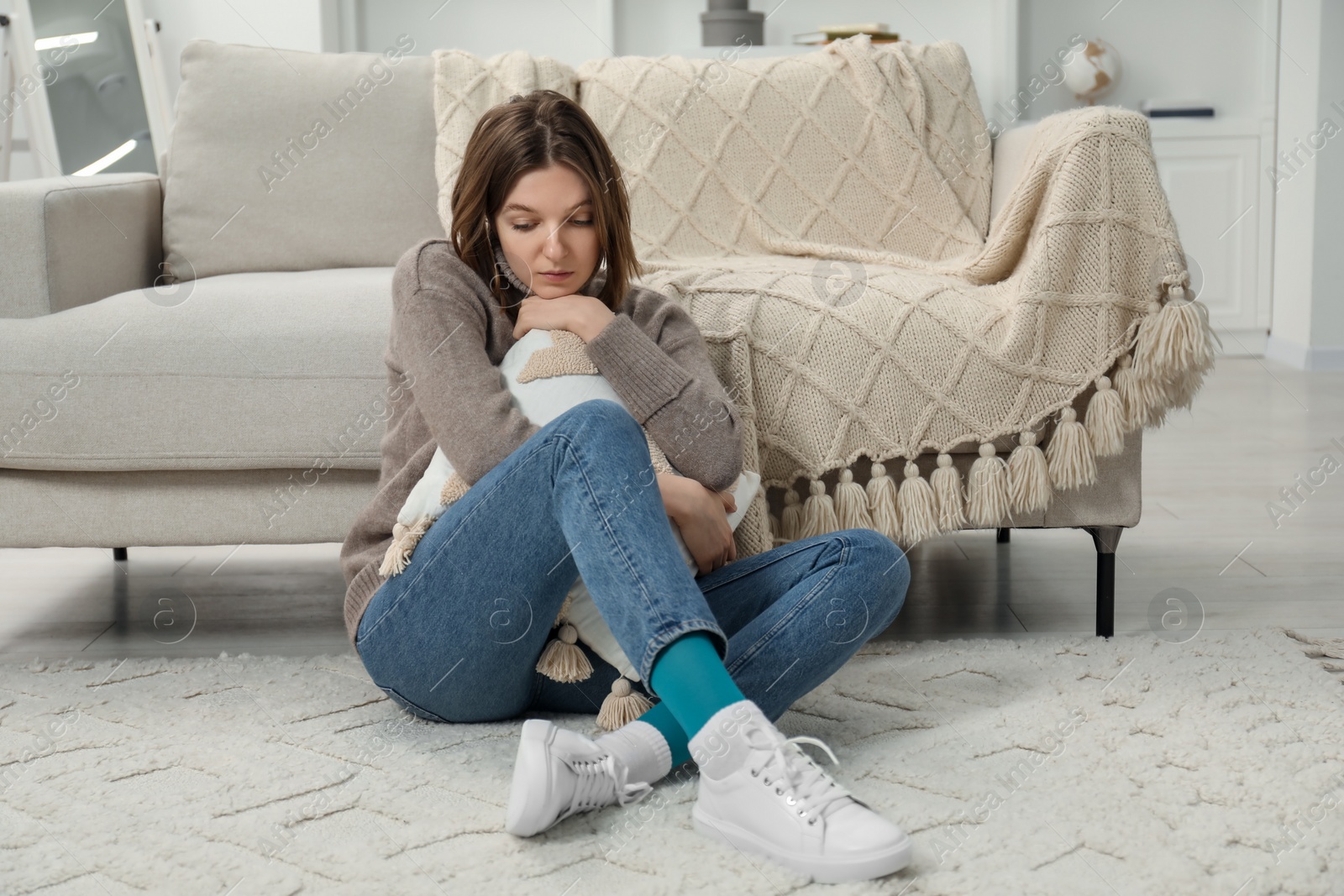 Photo of Sad young woman sitting on floor at home