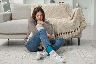Sad young woman sitting on floor at home