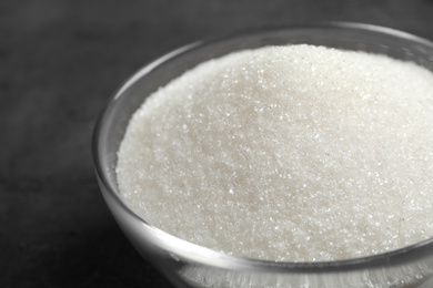 Photo of Granulated sugar in bowl on grey table, closeup