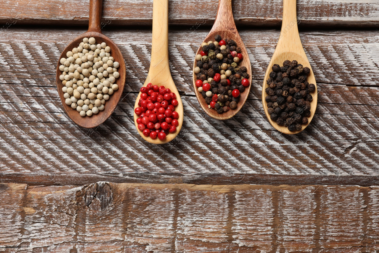 Photo of Aromatic spice. Different peppers in spoons on wooden table, flat lay. Space for text