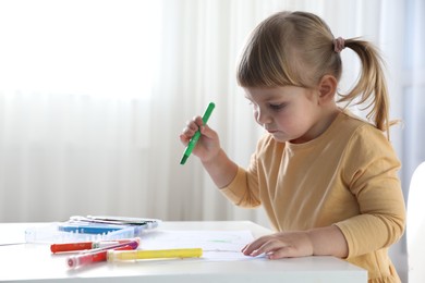 Cute little girl drawing with marker at white table indoors. Child`s art