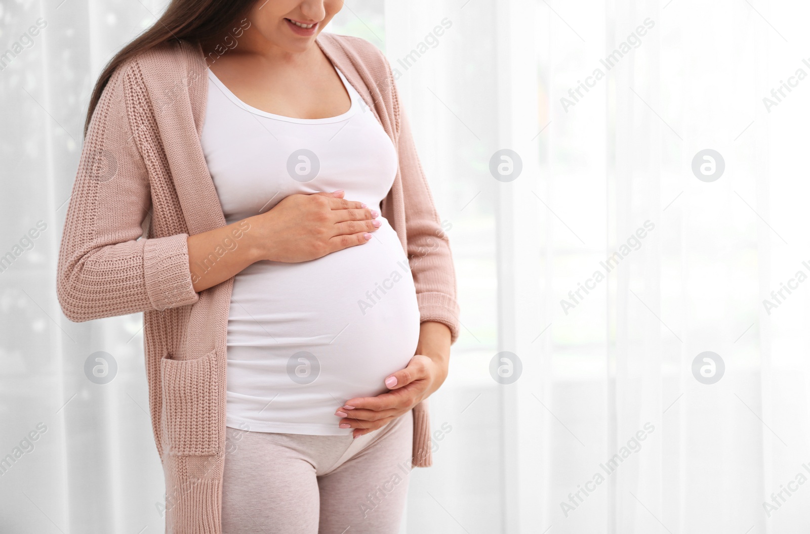 Photo of Young pregnant woman near window at home, closeup