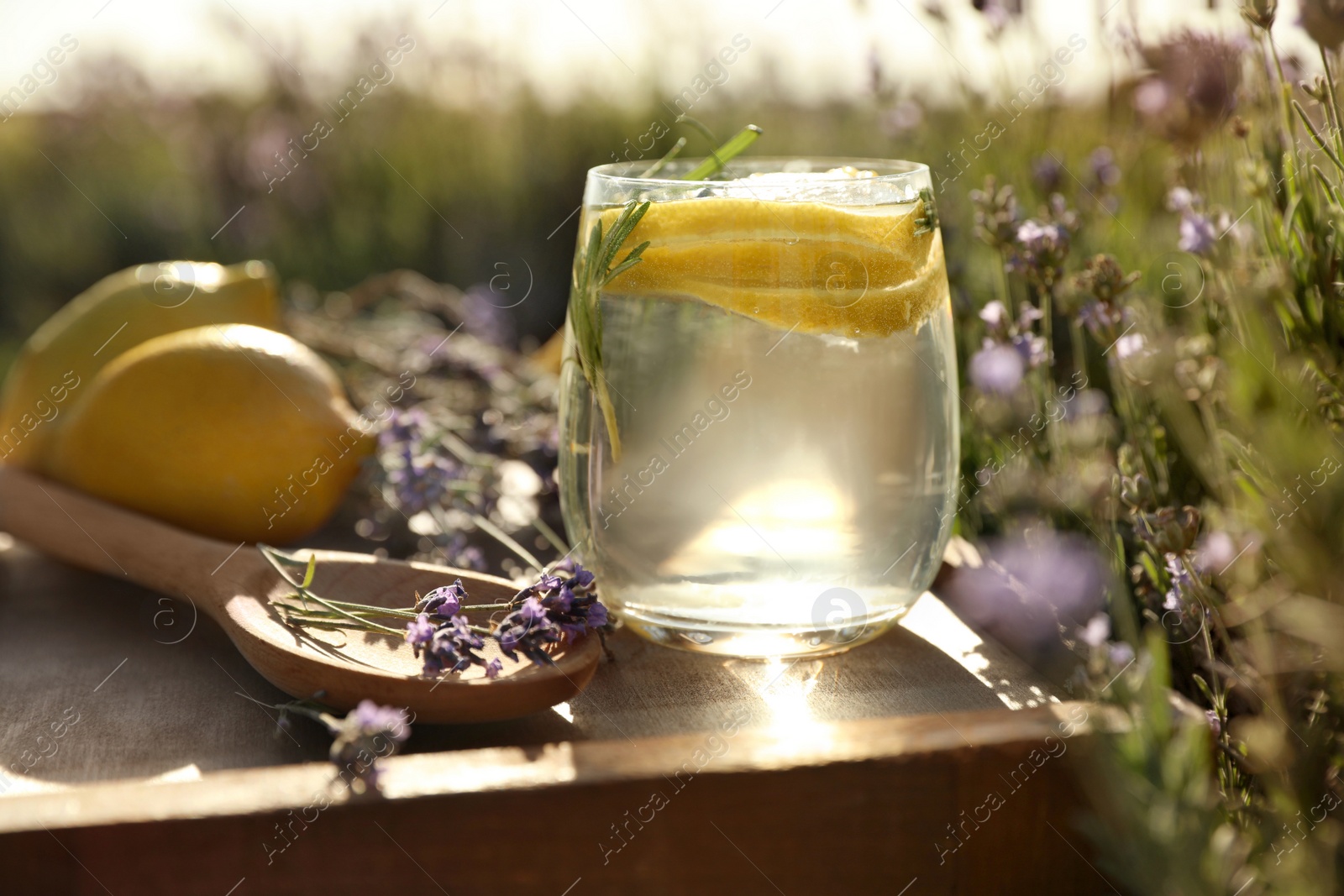 Photo of Glass of fresh lemonade on wooden tray in lavender field